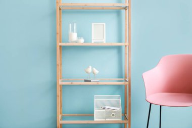 Dekorlu ahşap raf ünitesi ve mavi duvarın yanında pembe koltuk.