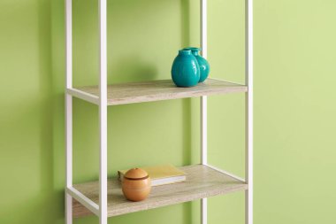 Vazolarla raflama ünitesi ve yeşil duvarın yanında kitap.