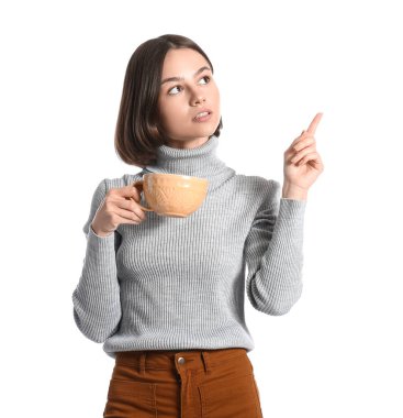 Elinde kahve fincanı olan güzel bir kadın beyaz arka plandaki bir şeyi işaret ediyor.