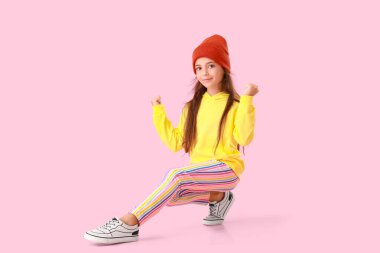 Sarı kapüşonlu sevimli küçük kız pembe arka planda dans ediyor.