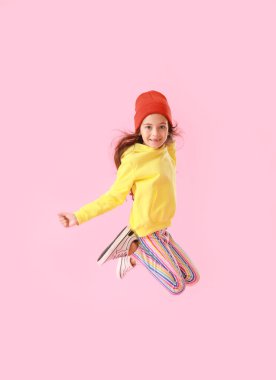 Sarı kapüşonlu sevimli küçük kız pembe arka planda zıplıyor