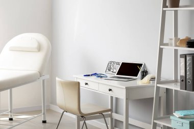 Doktorun iş yerinde, muayenehanedeki ışık duvarının yanında dizüstü bilgisayarı vardı.