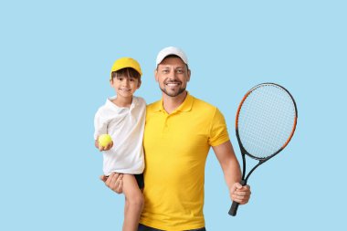 Mavi arka planda tenis raketi olan küçük çocuk ve antrenörü.