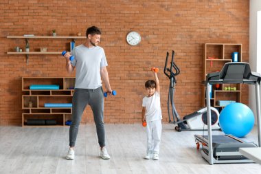 Küçük çocuk ve kanepede spor salonunda dambıllarla antrenman yapıyor.