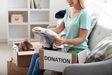 Genç bir kadın bağış için kıyafetlerini kutuya koyuyor.