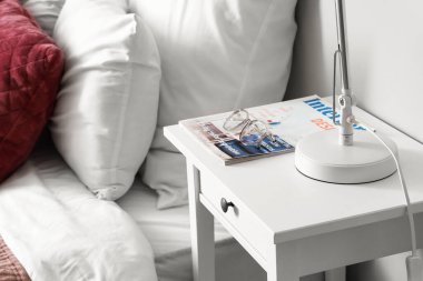 Yatağın yanındaki masada gözlük ve şarjör var.