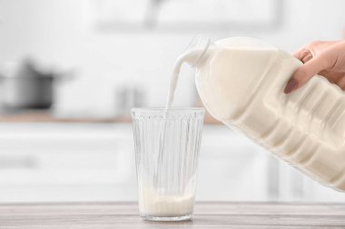 Kadın mutfaktaki masaya bir galon sütü bardağa boşaltıyor.