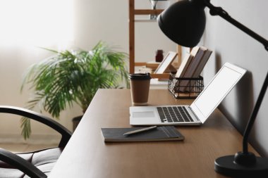 Ofis duvarının yanında dizüstü bilgisayarı ve kahve fincanı olan modern bir iş yeri.
