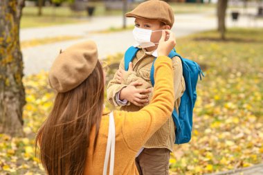 Okuldan önce küçük oğlunun maskesini takmasına yardım eden bir kadın.