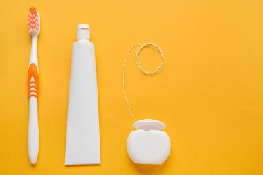 Diş ipi, diş macunu ve turuncu arka planda fırça.