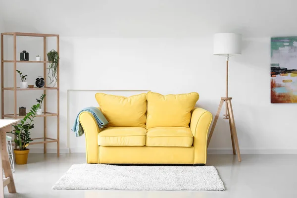 Interior of light living room with yellow sofa, shelving unit and plants