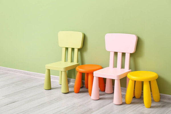 Different chairs and stools for children near color wall