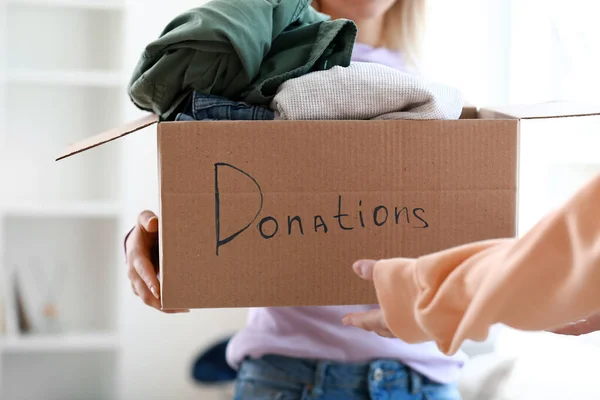 Young woman donating clothes in box at home
