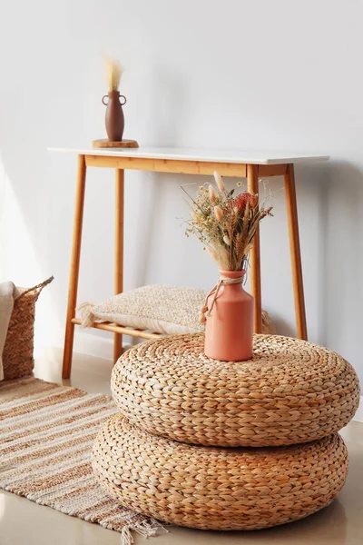 Vase with dried flowers on rattan poufs in light room