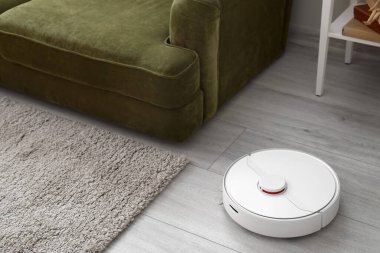 Odanın ahşap zemininde modern robot elektrikli süpürge.