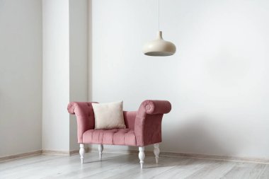 Yastıklı pembe koltuk ve ışık duvarının yanında asılı lamba.