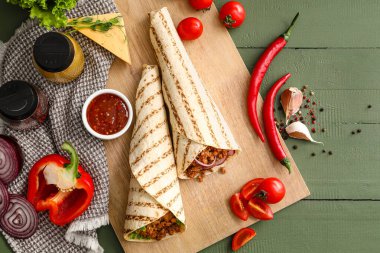 Lezzetli burritoları, sebzeleri ve baharatları olan ahşap renkli bir masa.