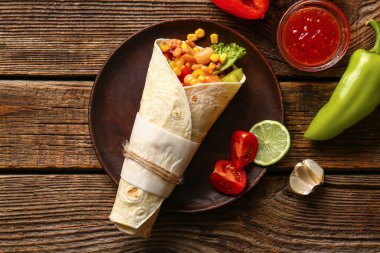 Tahta arka planda sebzeli bir tabak lezzetli Meksika dürümü.