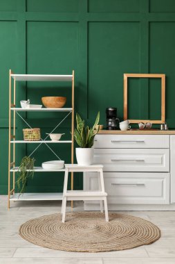 Beyaz tezgahı, raf ünitesi ve yeşil duvarı olan şık bir mutfak.