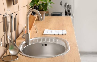 Mutfakta bej duvarın yanında gümüş lavabo olan ahşap tezgah.