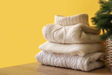 Masanın üzerinde renkli arka planda Noel ağacı olan sıcak süveterler.