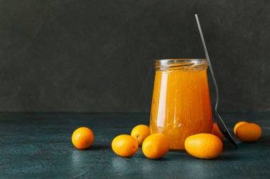 Lezzetli kumkat reçeli kavanozu ve siyah arka planda taze meyveler.
