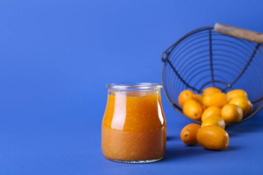 Lezzetli kumkat reçeli kavanozu ve mavi arka planda taze meyveler.