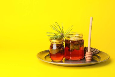 Sarı arka planda lezzetli kozalak reçeli kavanozlarıyla dolu bir tabak.