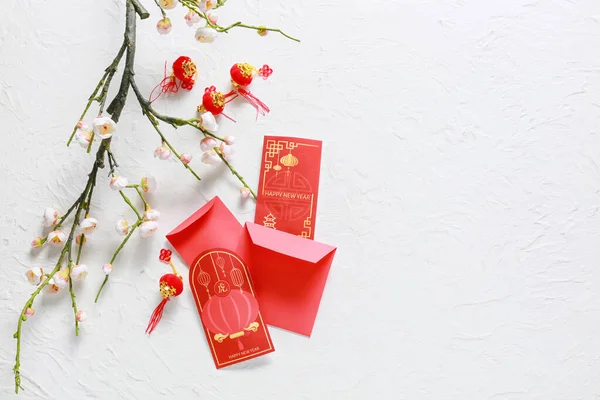 Üzerinde Çin fenerleri ve beyaz arka planda çiçek açan erik dalları olan kırmızı zarflar. Yeni yıl kutlaması