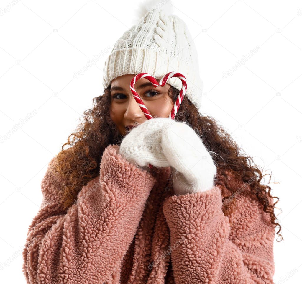 Beautiful young woman in stylish winter clothes and with candy canes on white background