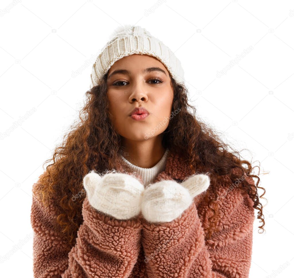 Beautiful young woman in stylish winter clothes sending air kiss on white background