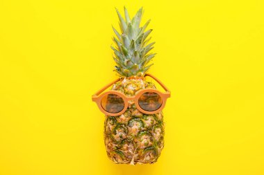 Sarı arka planda güneş gözlüklü taze ananas.