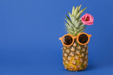 Mavi arka planda çiçek olan güneş gözlüklü komik ananas.
