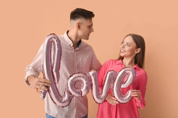色の背景に単語の愛の形で風船を持つ若いカップル バレンタインデーのお祝い — ストック写真