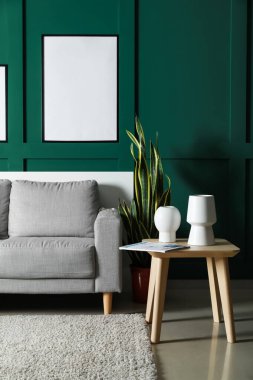 Modern oturma odasındaki yeşil duvarda boş posterler asılı. Kanepe ve çiçekli.