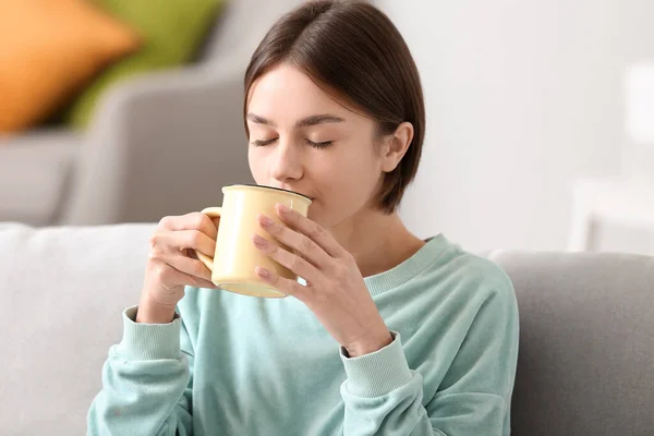 漂亮的年轻女子在家里沙发上喝着美味的茶 — 图库照片