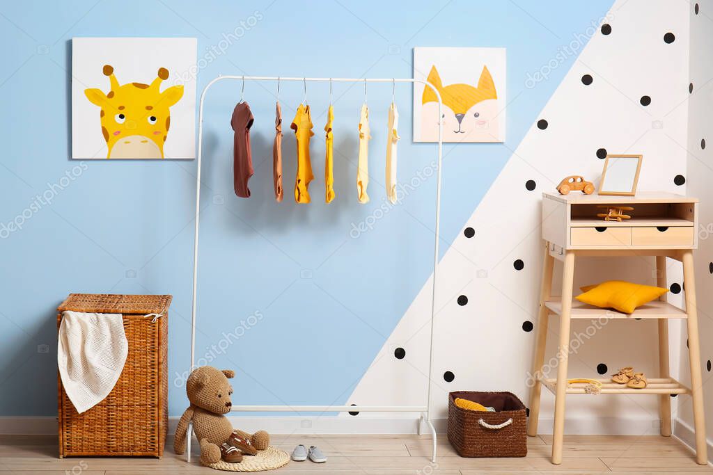Interior of stylish children's room with rack, baby bodysuits and table