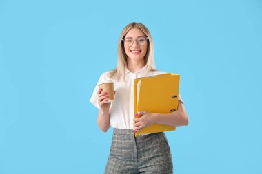 Mavi arka planda klasörü ve bir fincan kahvesi olan güzel genç bir kadın.