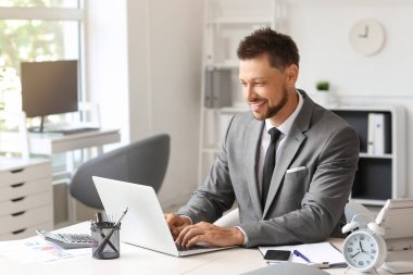 Ofisteki bilgisayarını kullanarak gülümseyen iş adamı.