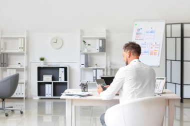 Ofiste hesap makinesiyle çalışan yakışıklı bir iş adamı.