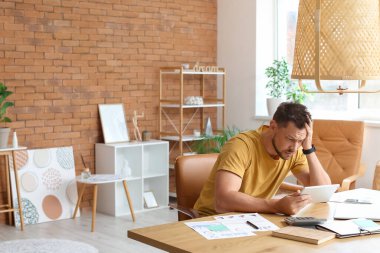 Ofiste tablet bilgisayarla çalışan stresli genç adam.