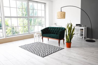 Yeşil kanepeli, çiçekli ve ayakta duran lambalı aydınlık oturma odasının içi.