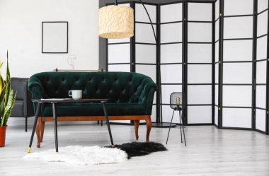 Yeşil kanepe, masa ve lambalarla aydınlık oturma odasının içinde.