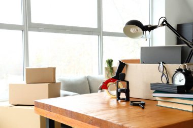 Taşındığı gün masada üzerinde eşyalar ve koli bandı olan karton kutu.