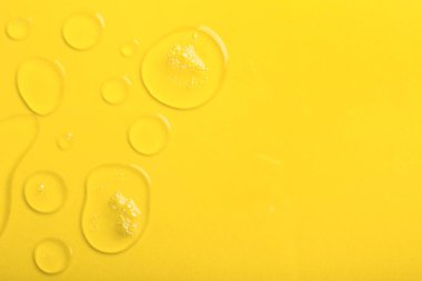 Sarı zemin üzerinde kabarcıklar olan saydam sıvı jel damlaları