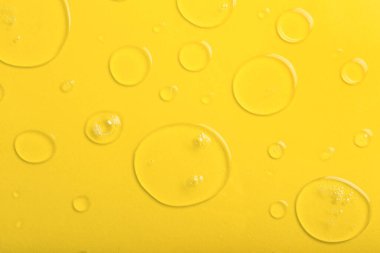 Sarı zemin üzerinde kabarcıklar olan sıvı şeffaf jel damlaları