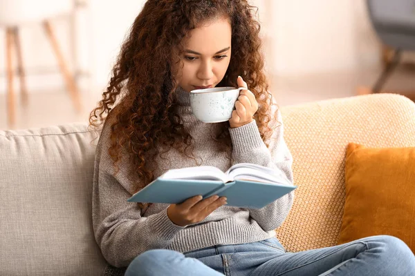 Genç Afro Amerikalı Kadın Evdeki Kanepede Kitap Okurken Çay Içiyor — Stok fotoğraf