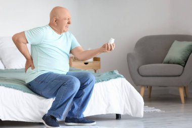 Yatak odasında sırt ağrısı çeken bir şişe haplı yaşlı adam.