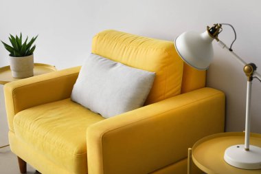 Sarı koltuk, lambalı kahve masaları ve ışık duvarının yanındaki çiçek.