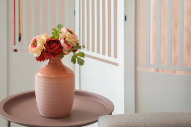 Katlanan ekranın yanındaki sehpanın üzerinde şakayık çiçekleri olan vazo.